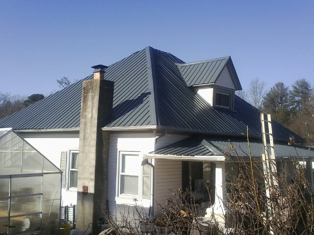 Dark blue standing seam metal roof on a white farmhouse with dormer — Slate & Tile Roof Repair by Roofing Brothers in Belle Haven