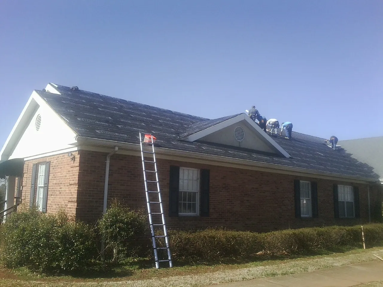 Crew tearing shingles off a brick ranch roof with a ladder set — Emergency Roof Repair work by our crew in Belle Haven