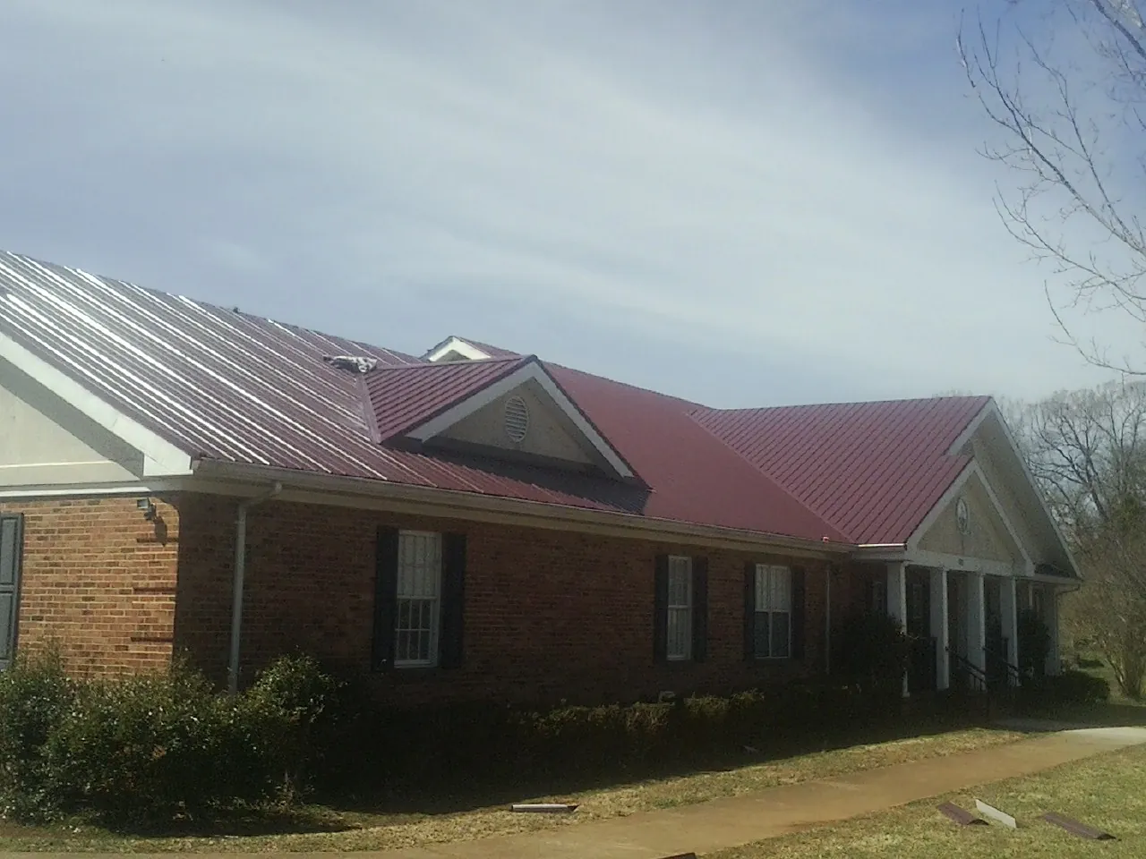 Red metal roof with gabled entries on a long brick building, from a Hail Damage Roof Repair job in Belle Haven