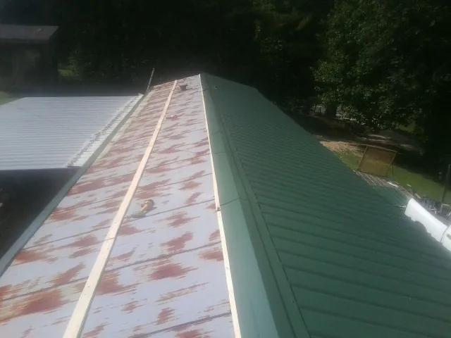 Old rusted panels beside newly installed green metal roofing — Wind Damage Roof Repair by Roofing Brothers in Belle Haven