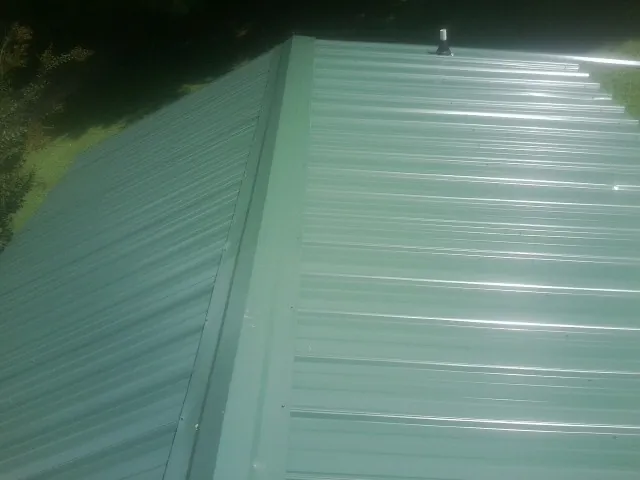 New green metal panels meeting at the ridge of a roof — Flat Roof Repair work by our crew in Belle Haven