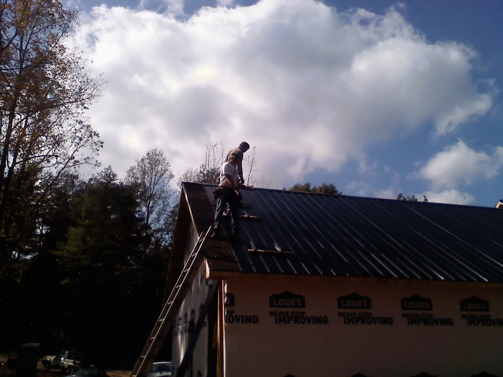 Roofer fastening dark metal panels high against a cloudy sky, from a Roof Inspection job in Belle Haven